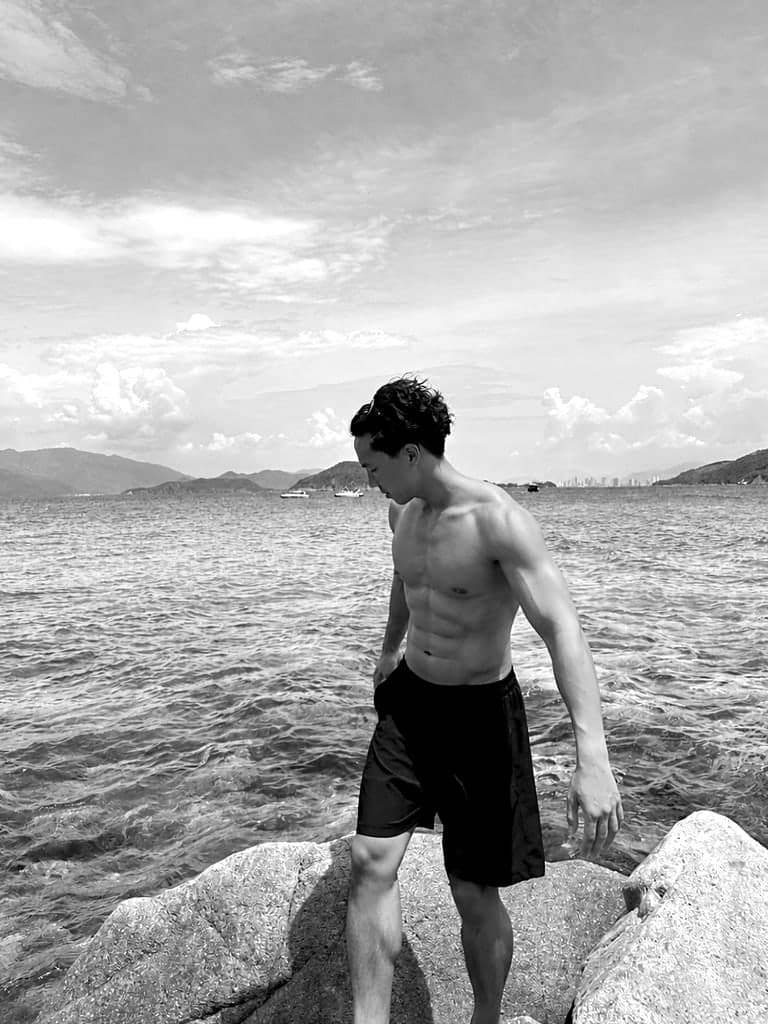 Black-and-white photo of Wilhelm Dang standing on rocks by the sea on the Vietnamese coast